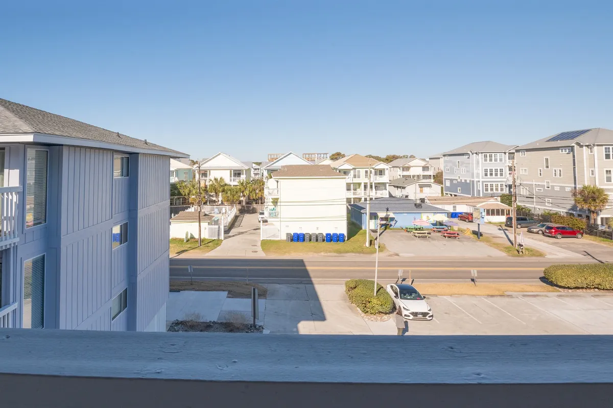 This view captures the surrounding neighborhood with palm trees, an open road leading toward the beach, and nearby buildings. It offers a sense of place and hints at nearby attractions, local exploration, and the leisurely pace of the community.
