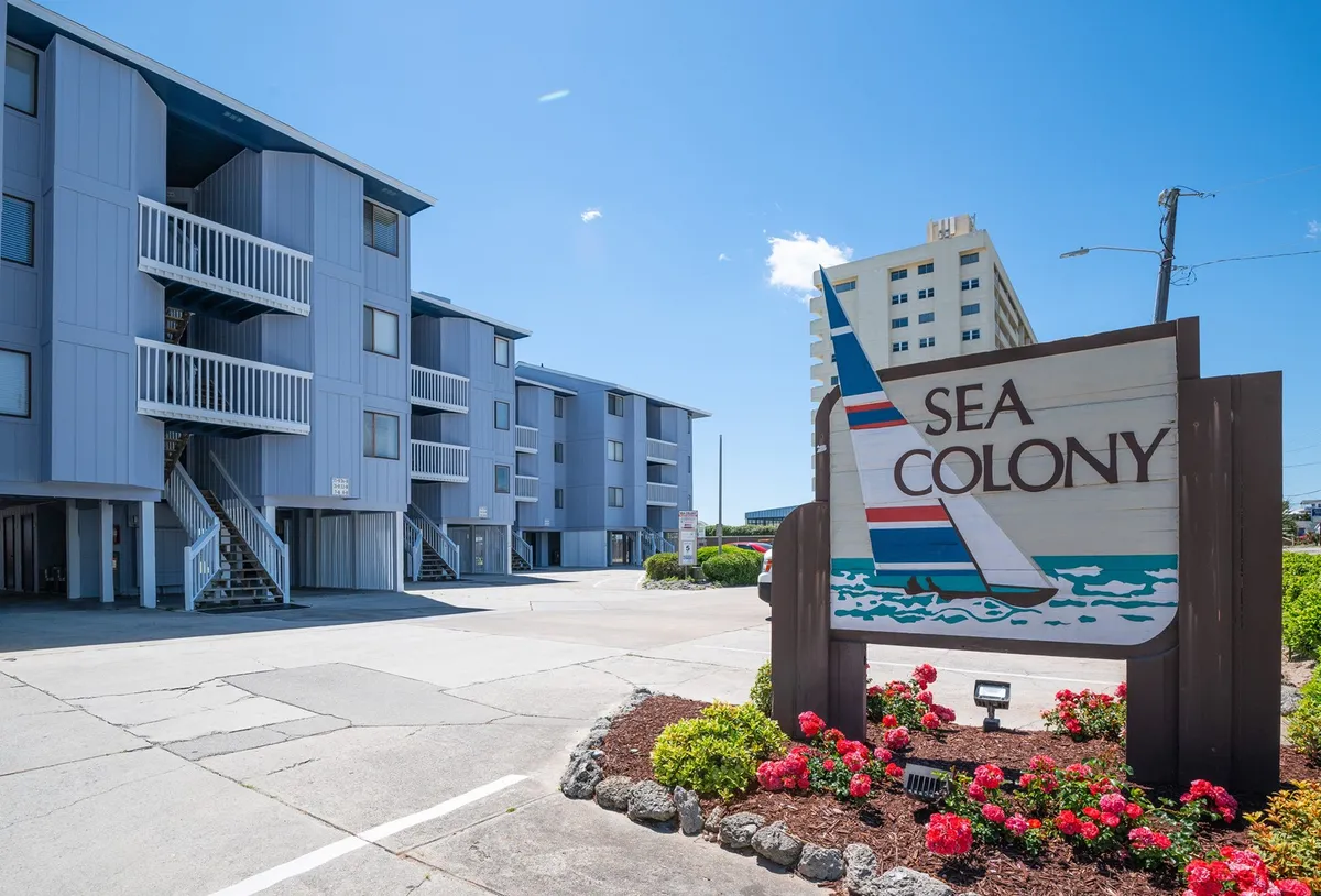 This image shows the exterior of the property, featuring a welcoming building facade surrounded by lush landscaping and visible signage. The inviting ambiance hints at well-maintained common areas, ideal for relaxing strolls or morning coffee while enjoying ocean breezes.