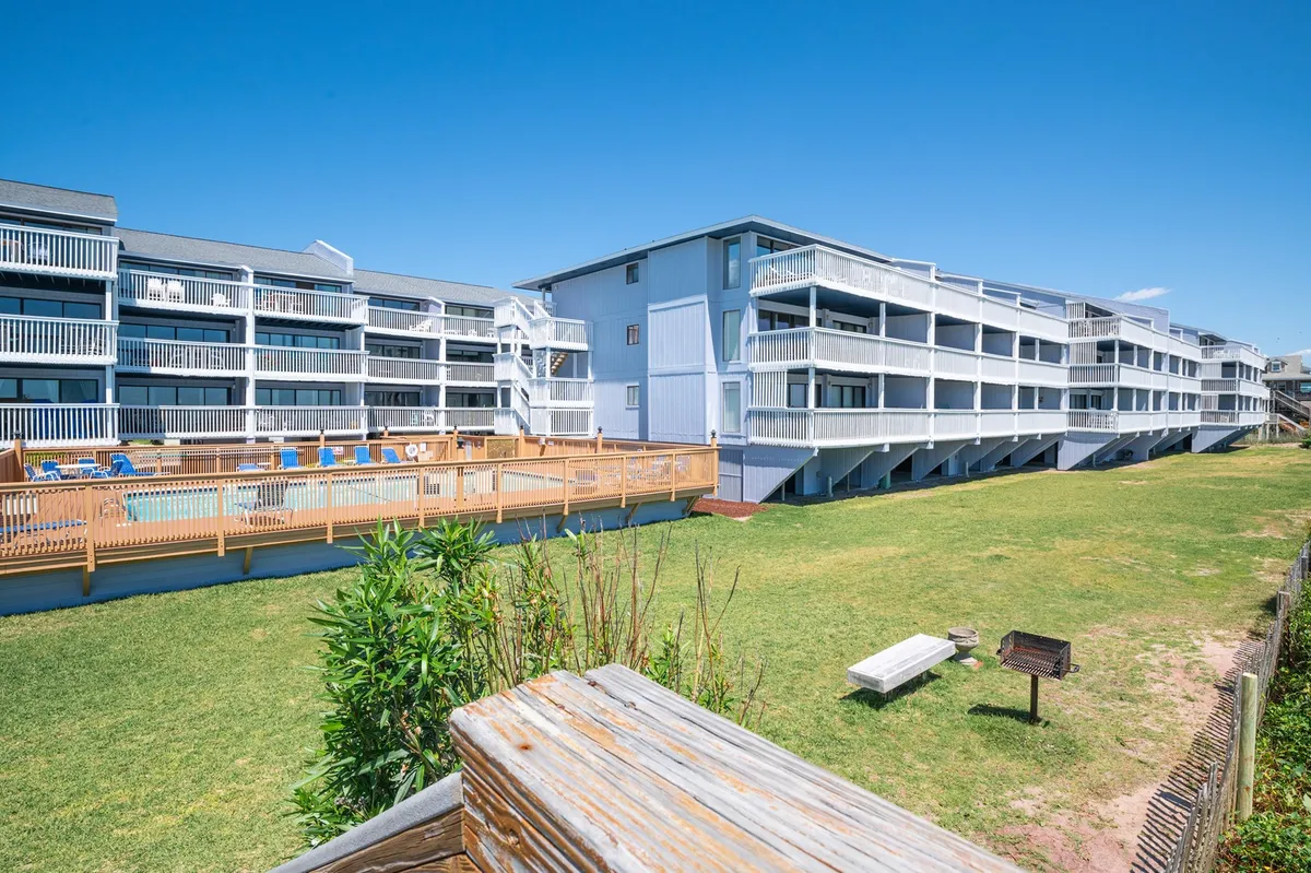 A relaxed exterior shot showing the swimming pool surrounded by a lawn area and balconies, signaling communal amenities and the inviting, sunlit outdoor spaces available for relaxation.