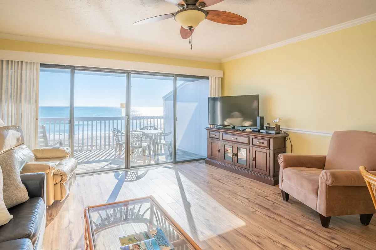This interior image features a comfortable living room with large sliding glass doors that open directly to an ocean view. The room is furnished with plush seating and a coffee table, while a TV unit sits opposite the seating area. Soft natural light fills the space, creating a tranquil and welcoming atmosphere conducive to relaxation, family movie nights, and enjoying the view.