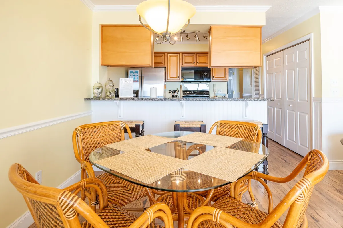 The dining area featuring a glass-topped dining table surrounded by woven chairs sits just beside the kitchen. The granite countertop is visible, tying the space to the kitchen, and the area exudes warmth—ideal for family gatherings and intimate meals.