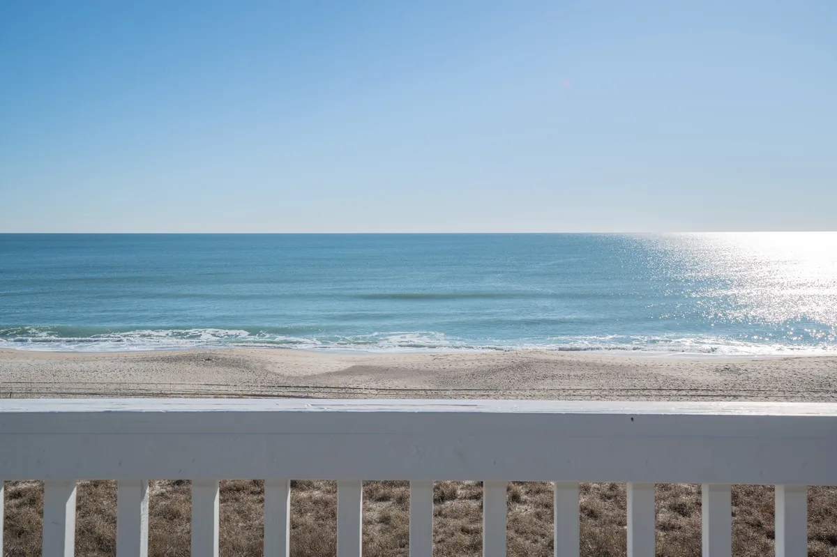An expansive, serene view of a calm ocean and sandy beach, with the distant horizon creating a sense of endless possibility. The scene is tranquil and inviting, perfect for hand-in-hand strolls or quiet reflection.