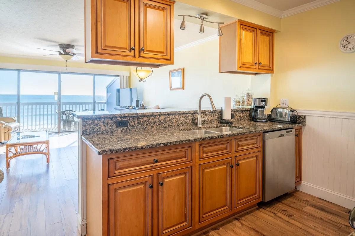 A welcoming kitchen with granite countertops, warm wooden cabinets, and modern stainless appliances. Sunlight streams through a window framing a stunning ocean view, while the breakfast bar invites casual conversation and morning meals.
