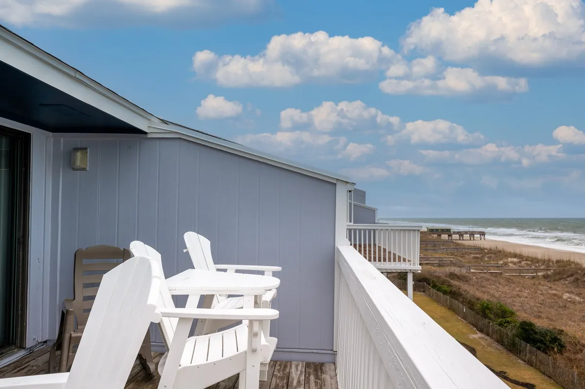 This image captures a pair of adirondack chairs facing the ocean on a private deck, with a serene view of the Atlantic just beyond the railing. The setting suggests a tranquil spot perfect for sipping morning coffee while watching the sunrise or enjoying a peaceful evening together.